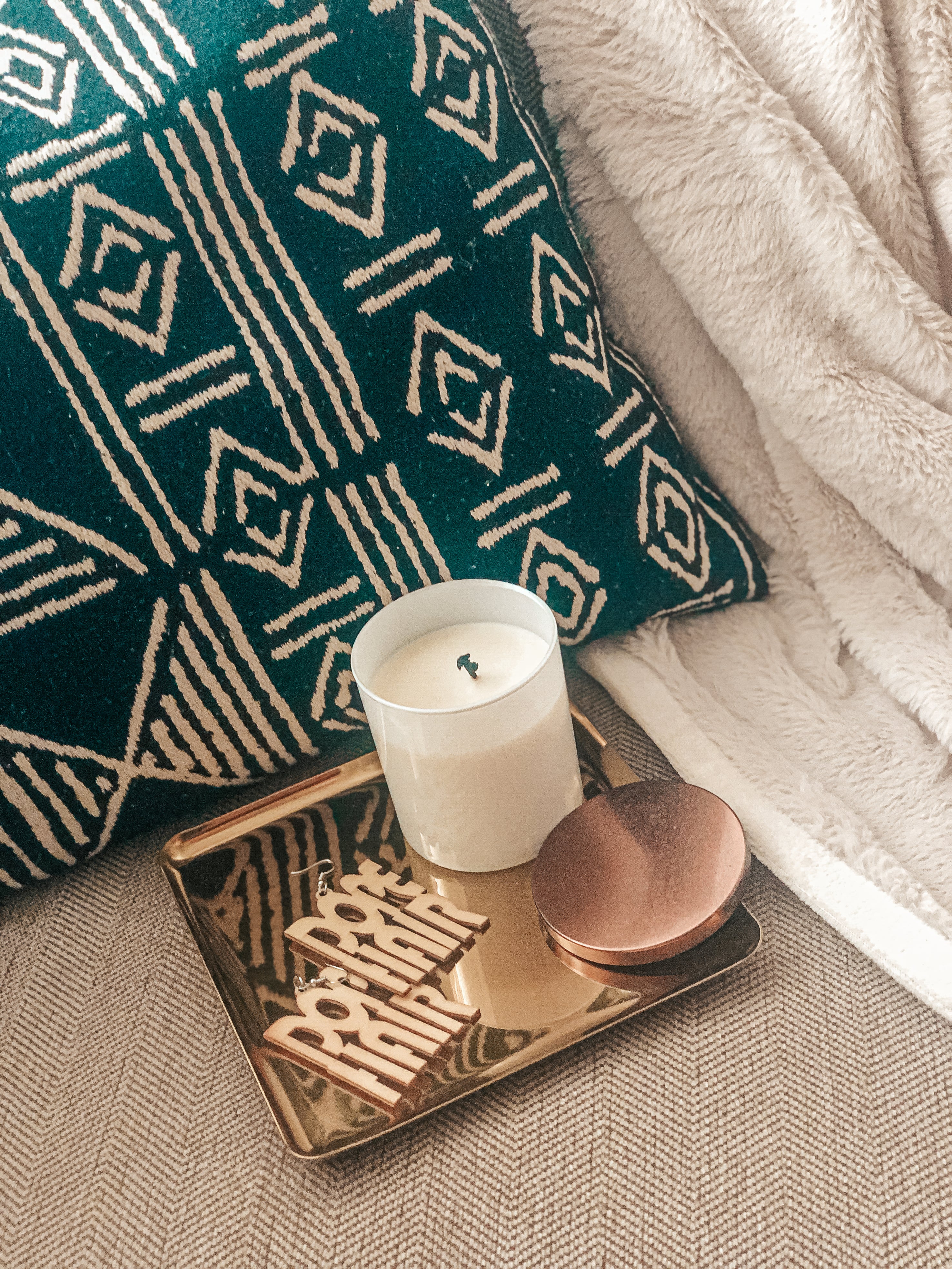 Scented coconut soy candle on a gold square tray with a fuzzy throw blanket. 